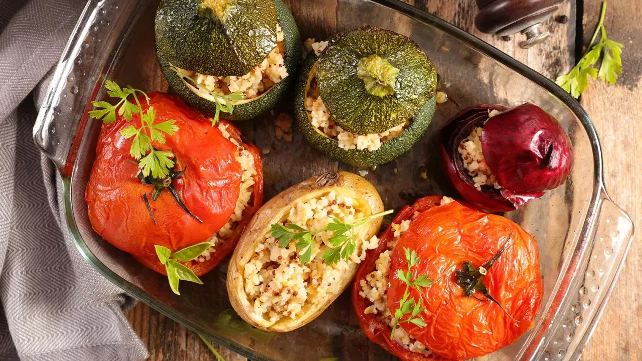 Plat de farce à légume : tomates, courgettes rondes, oignon rouge et pomme de terre farcis de grains, joliment présentés dans un plat en verre.