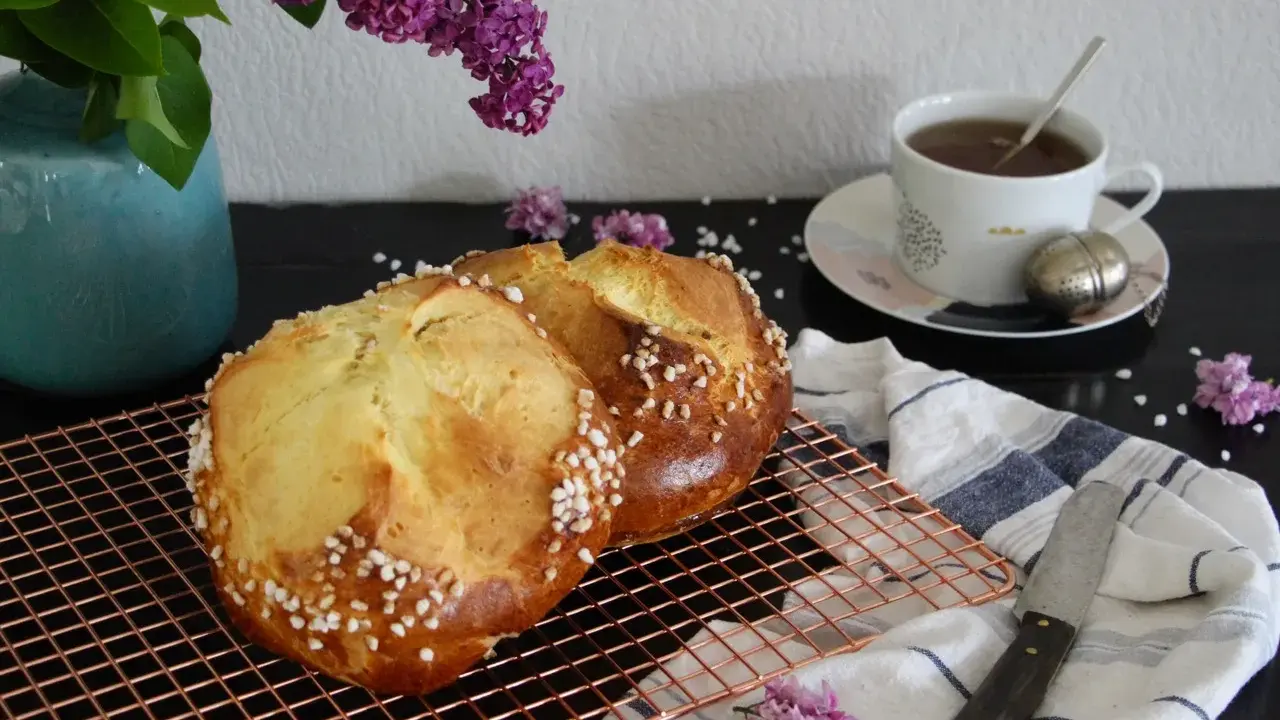 Deux pains briochés, parfaits pour une mouna recette, refroidissent sur une grille. Une tasse de thé et des lilas complètent la scène.