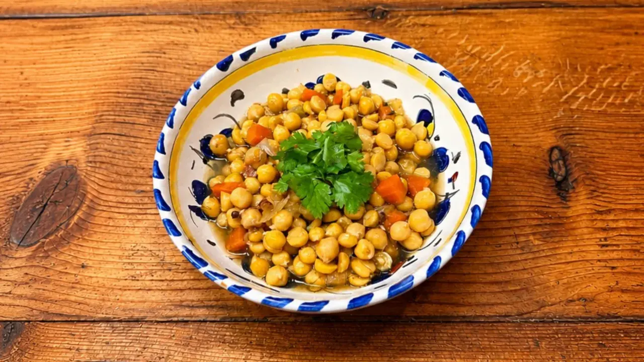 Un plat de pois chiches cuisinés avec des carottes et des oignons, garni de coriandre fraîche. La cuisson pois chiche est réussie, le plat est appétissant.
