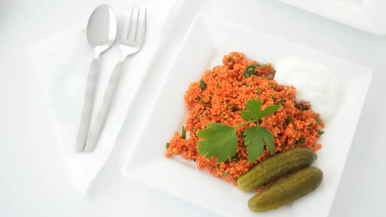 Un plat de boulgour coloré, garni de persil frais, servi avec des cornichons et une touche de yaourt. La cuisson du boulgour est parfaite pour ce repas.
