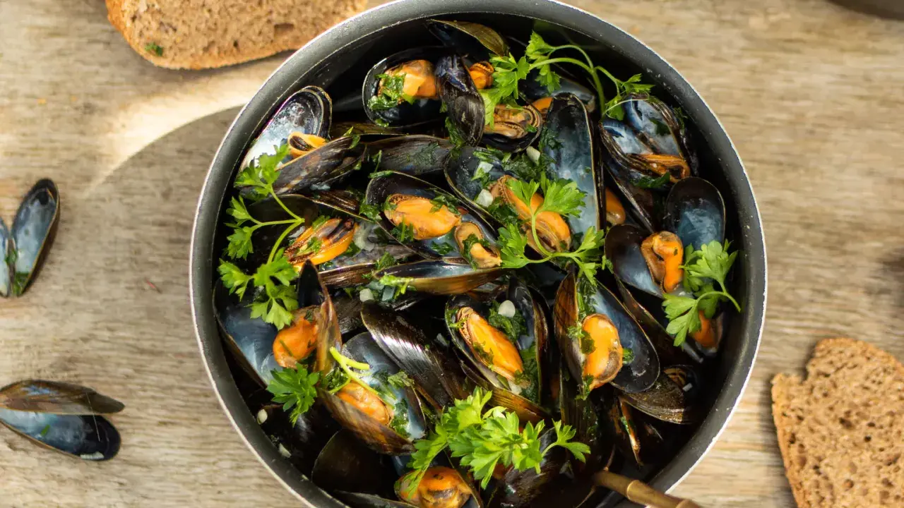 Un plat généreux de moules marinières, garni de persil frais, avec du pain de campagne à côté.