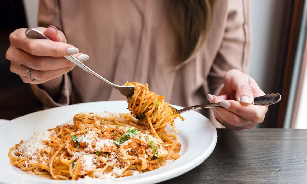 Une personne mange des spaghettis à la sauce tomate et au parmesan avec deux fourchettes.
