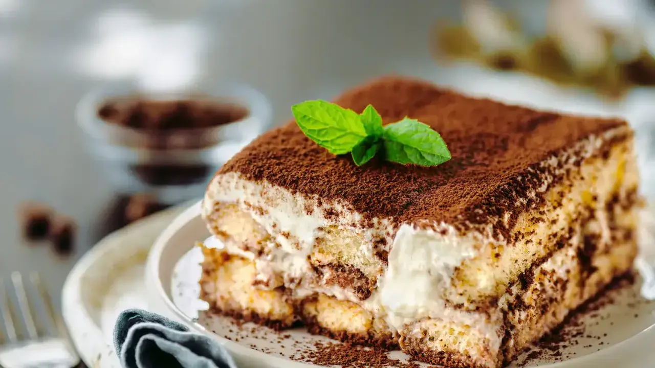 Un délicieux tiramisu anniversaire, saupoudré de cacao et garni d'une feuille de menthe fraîche, prêt à être dégusté.