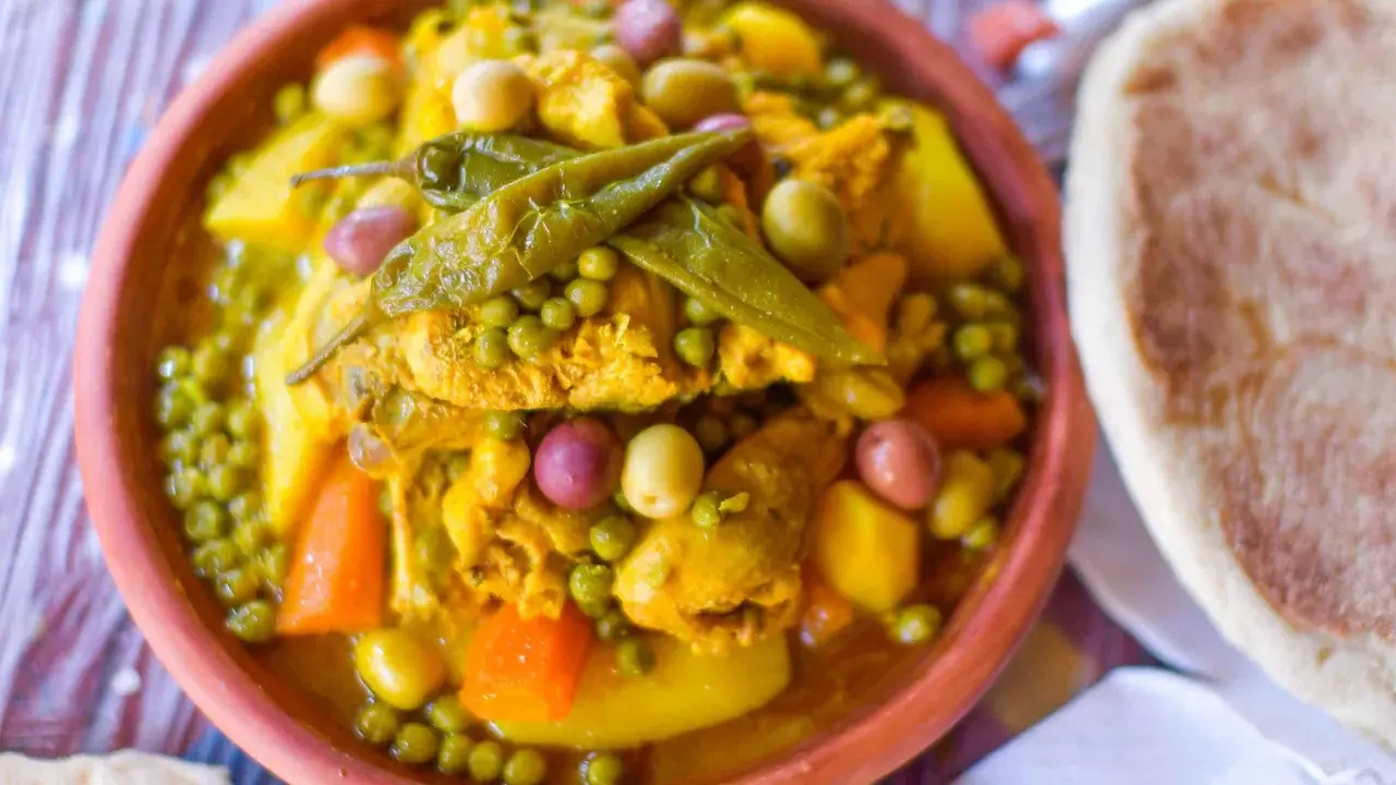 Un plat de tajine poulet aux olives, petits pois et carottes, garni de piments verts. Accompagné de pain.