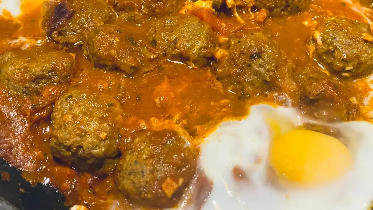 Un plat de tajine kefta oeuf mijote dans une sauce tomate épicée, avec des œufs pochés.
