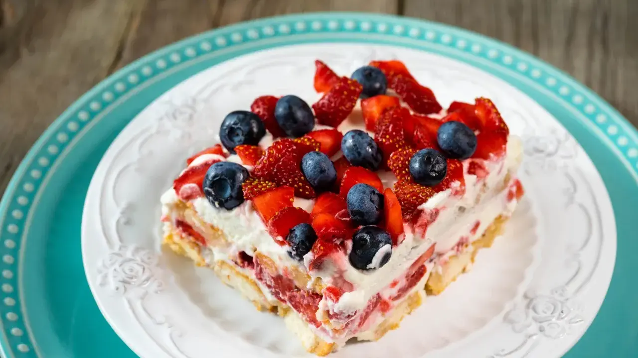 Tranche de tiramisu aux fruits rouges, garnie de fraises et myrtilles fraîches, sur une assiette blanche ornée.