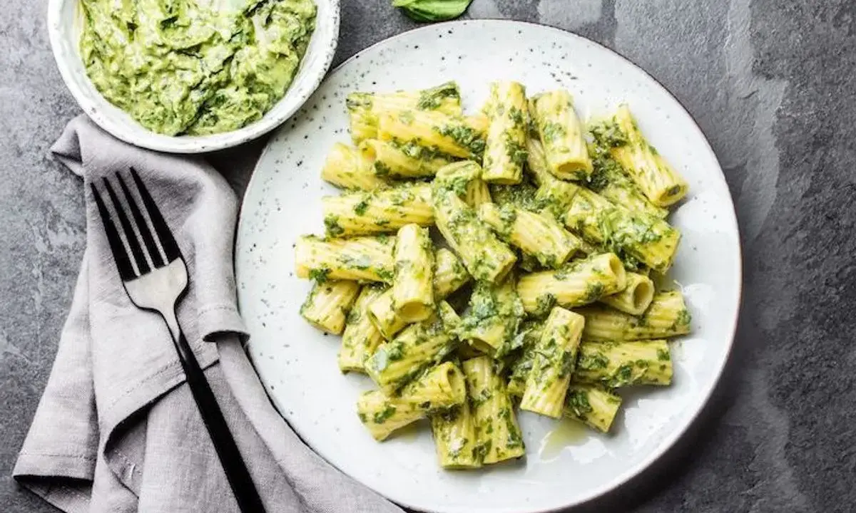 Assiette de pâtes rigatoni généreusement enrobées de pesto vert vif, avec un bol de sauce à côté. Un délice de pâtes au pesto !