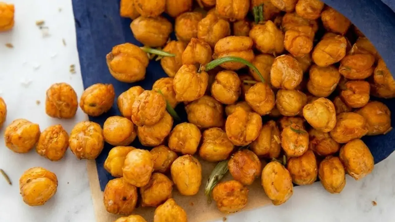 Un tas de pois chiches grillés dorés, certains tombant d'un sac bleu, avec des brins de romarin.