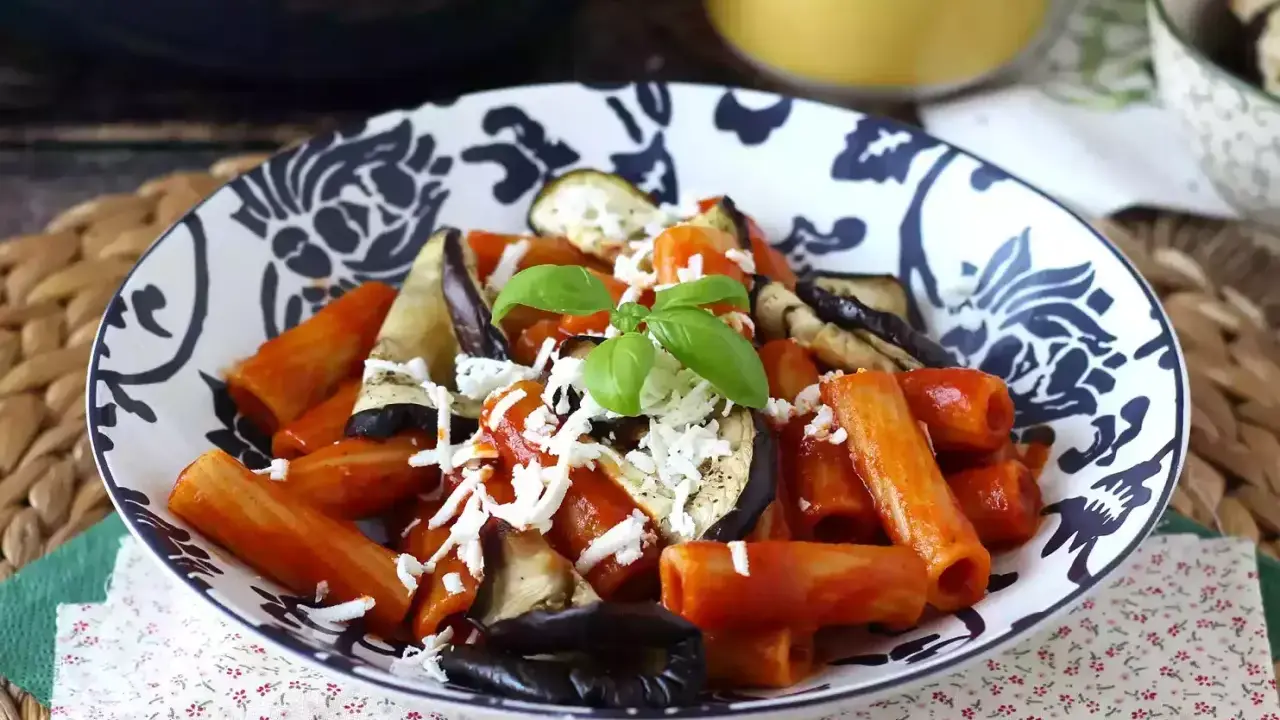 Pâtes rigatoni généreusement garnies de sauce tomate, d'aubergines grillées et de fromage râpé, le tout surmonté d'une feuille de basilic frais. Un plat de pâtes aubergines appétissant.