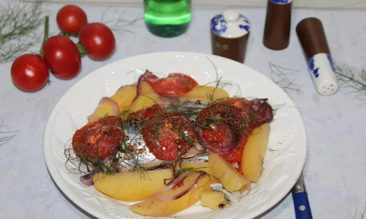 Maquereau au vin blanc, pommes de terre, tomates et oignons sur une assiette blanche.