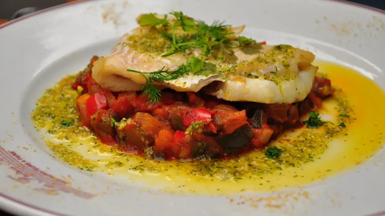 Délicieux dos de cabillaud à la poêle, servi sur un lit de légumes méditerranéens et arrosé d'une sauce verte.
