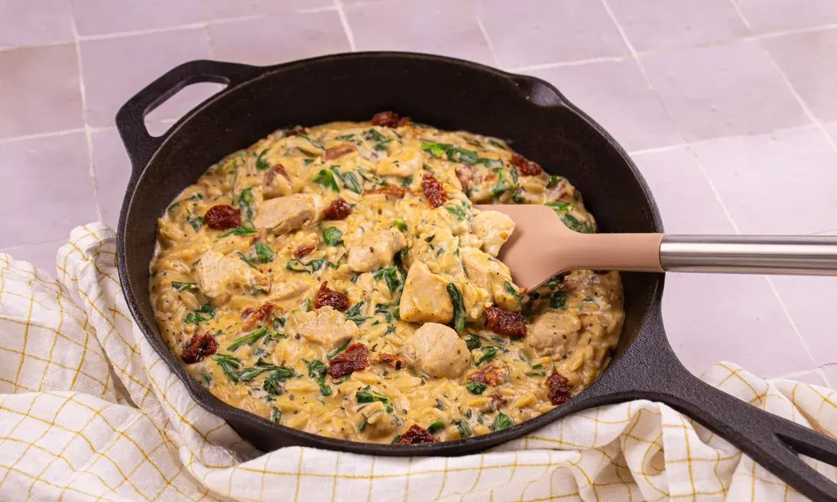 Un plat réconfortant de one pot orzo avec poulet, épinards et tomates séchées, servi dans une poêle en fonte.