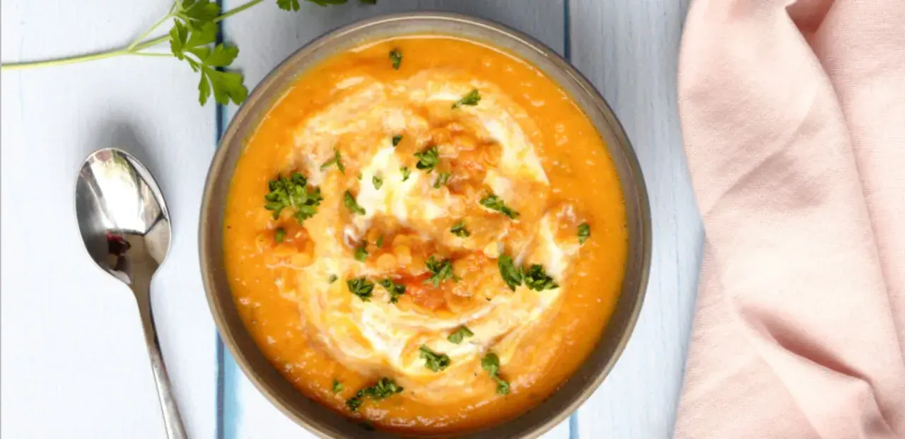 Un bol de soupe crémeuse aux lentilles corail, garni de crème et de persil frais, prêt à être dégusté avec une cuillère.