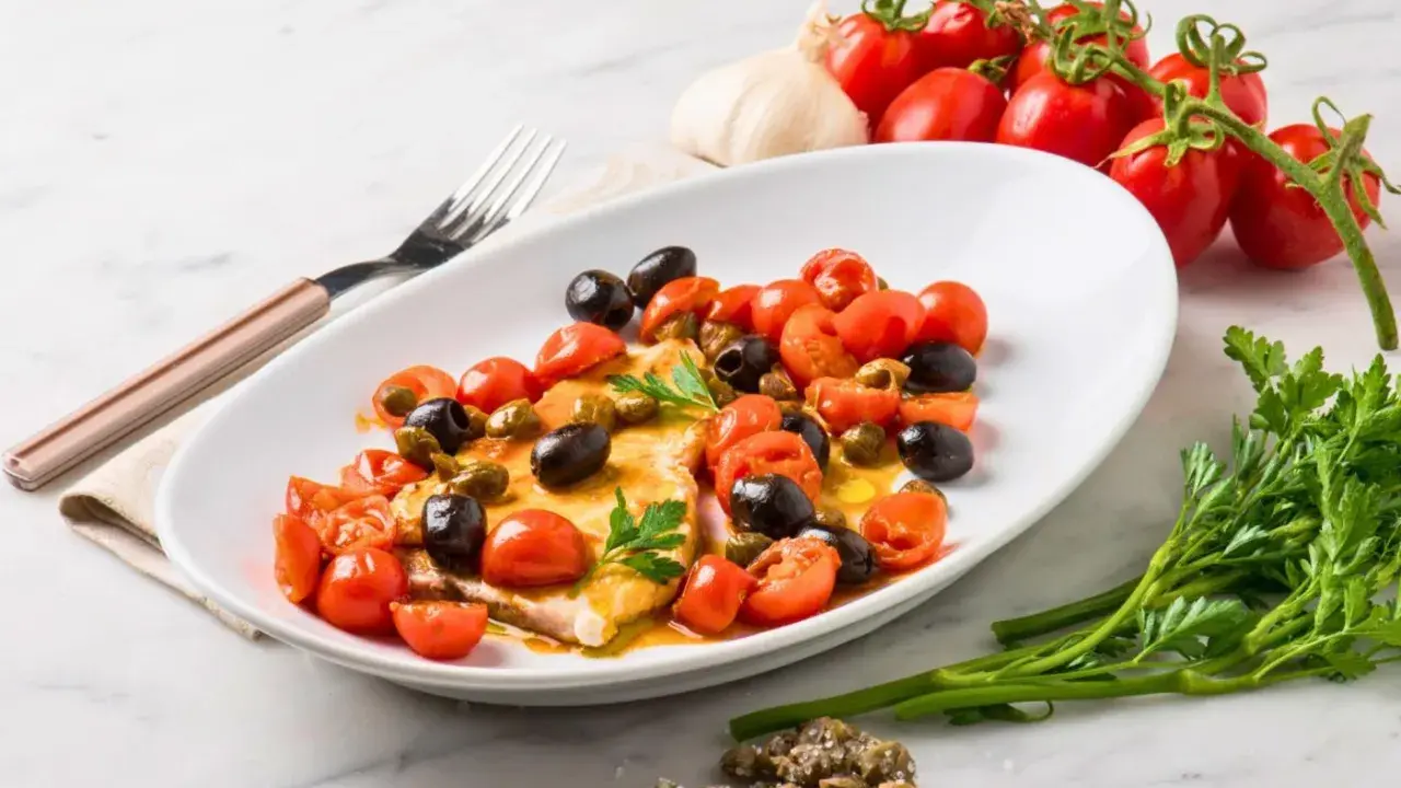 Filet de merlan servi avec tomates cerises, olives noires et câpres. Une assiette colorée et savoureuse.