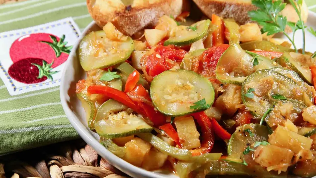 Un plat de légumes mijotés, rappelant un pisto manchego, avec des courgettes, poivrons et tomates, servi avec des toasts grillés.