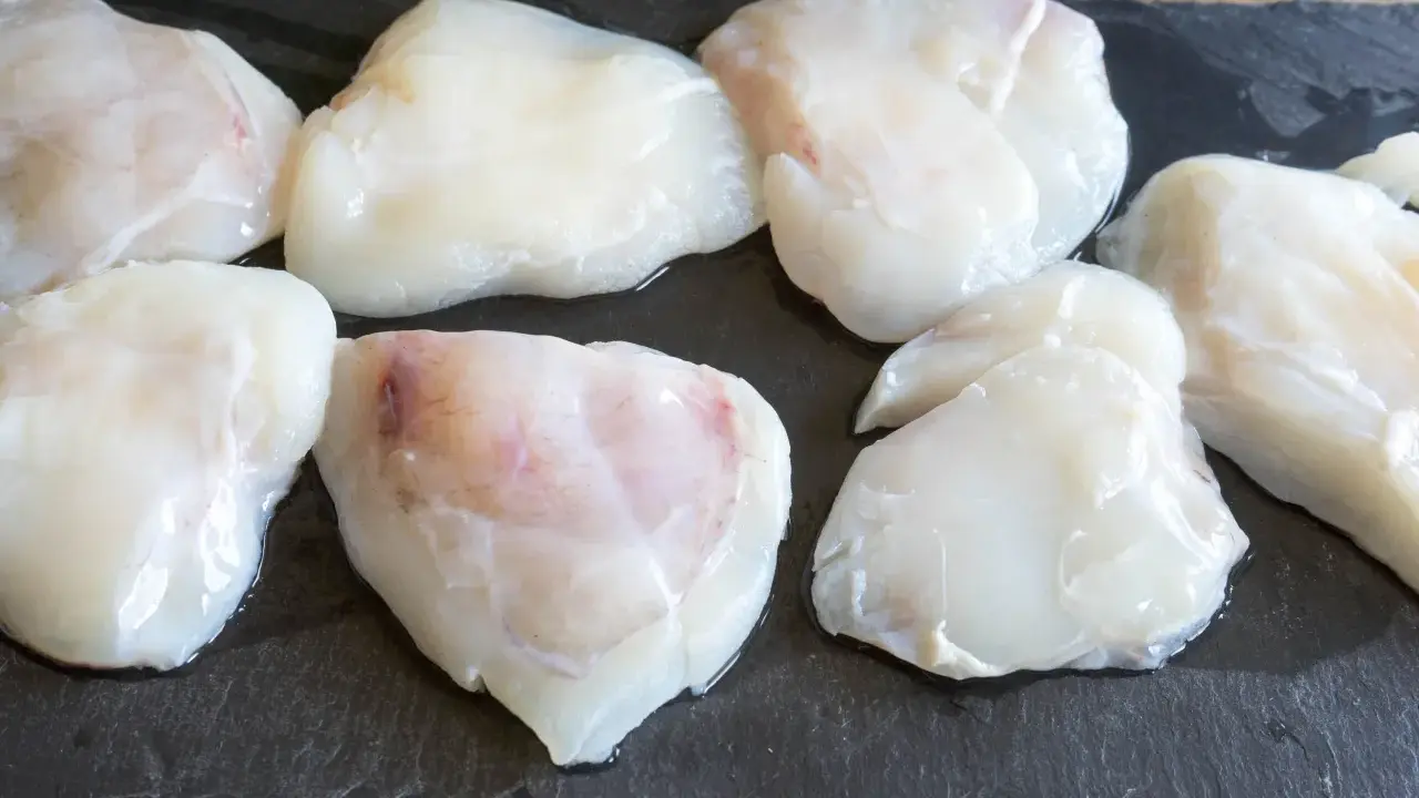 Plusieurs morceaux de lotte crue, prêts pour une cuisson au four, sont disposés sur une planche d'ardoise.