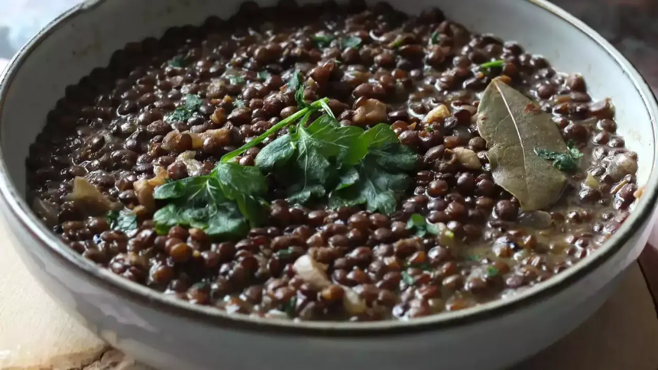 Un plat de cuisson lentilles vertes, garni de persil frais et d'une feuille de laurier. Un délice simple et réconfortant.