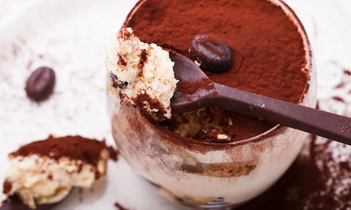 Un déliceux tiramisu cacao, saupoudré de cacao, avec une cuillère pleine de crème onctueuse et un grain de café.