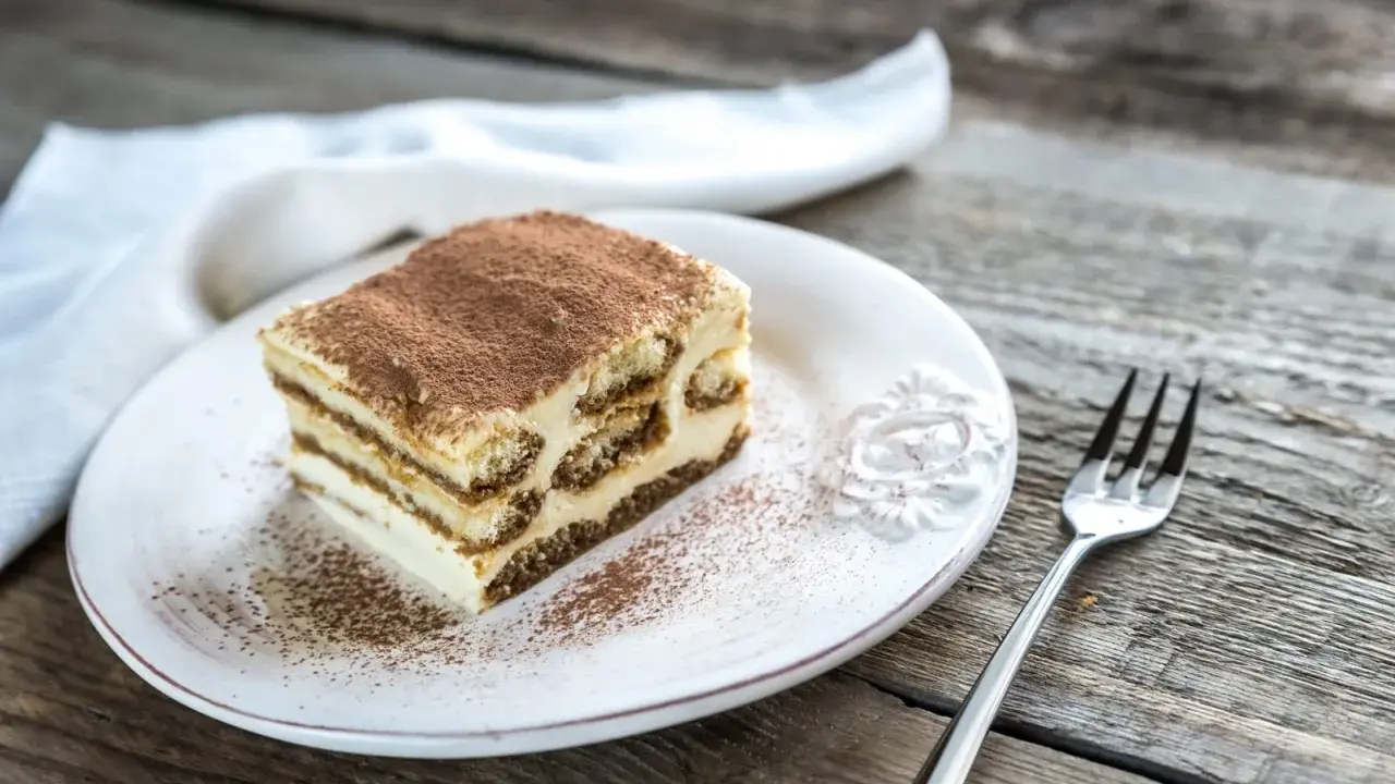 Une part de tiramisu maison, saupoudrée de cacao, sur une assiette blanche, prête à être dégustée. La conservation de ce délice est essentielle pour en savourer chaque bouchée.
