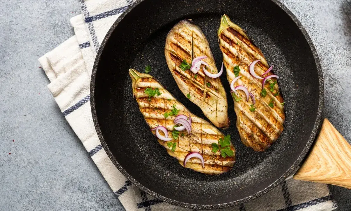 Aubergines grillées dans une poêle, garnies d'oignons rouges et de persil. Une délicieuse recette aubergine prête à être dégustée.
