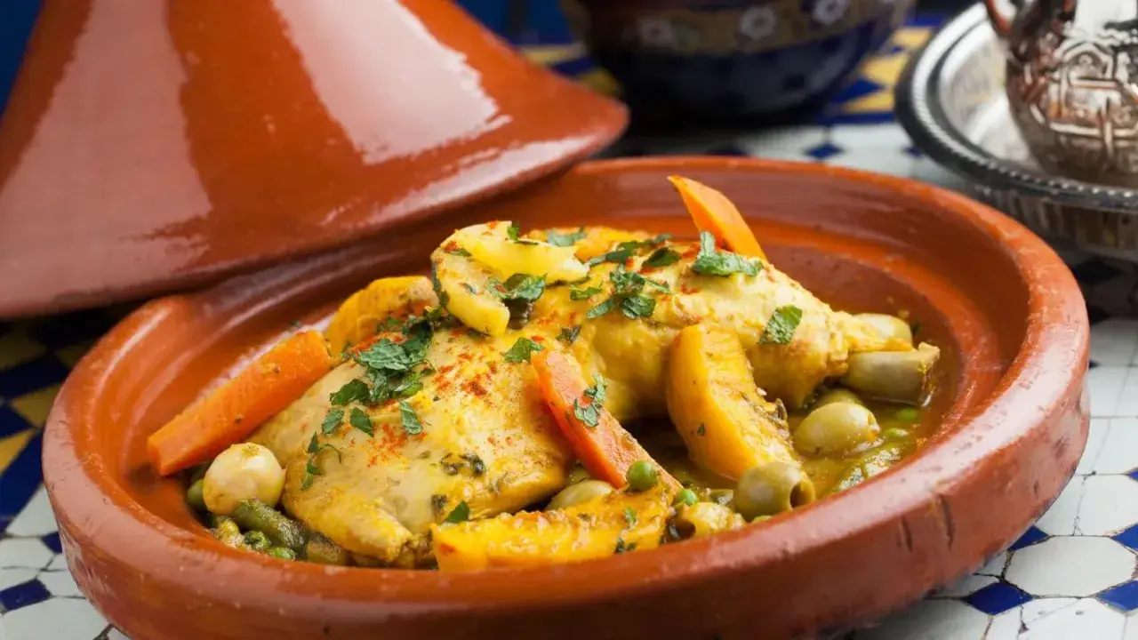 Un plat de tajine recette traditionnelle, avec du poulet, des carottes, des olives et des abricots, garni de persil frais.