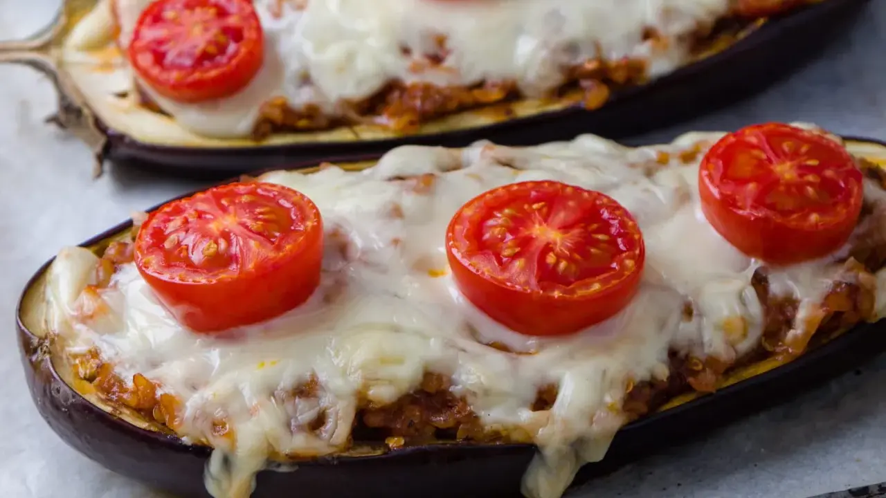 Deux aubergines farcies, garnies de tomates et de fromage fondu, prêtes à être dégustées.