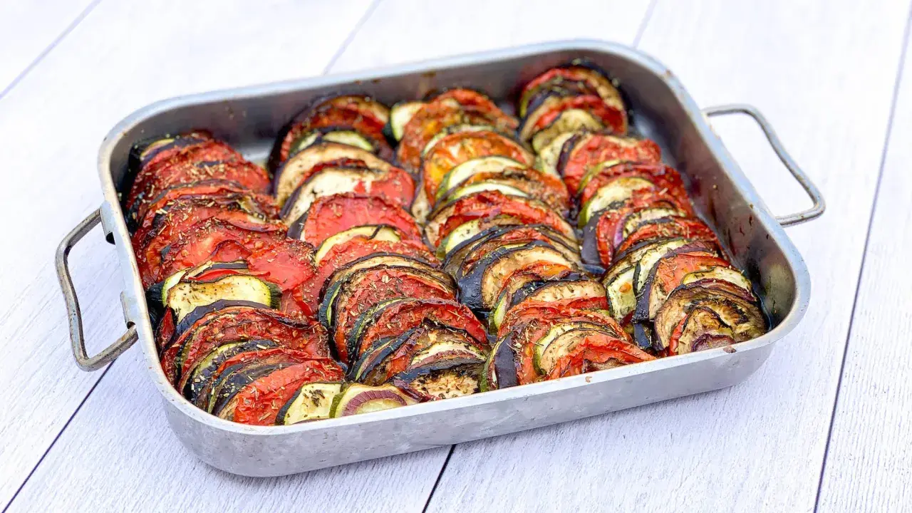 Un plat de tian de légumes, joliment arrangé en rondelles alternées de tomates, courgettes et aubergines, prêt à être dégusté.