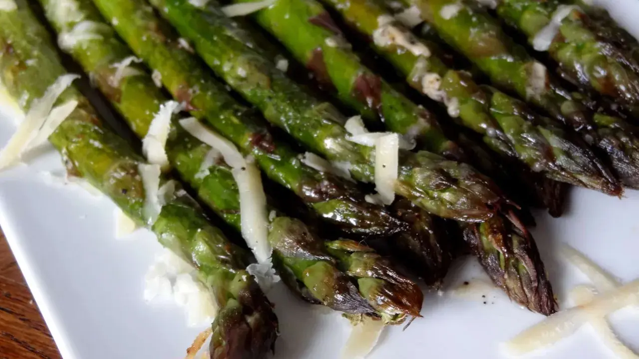 Un plat d'asperges au four, tendres et légèrement grillées, parsemées de copeaux de parmesan. Un délice simple et savoureux.