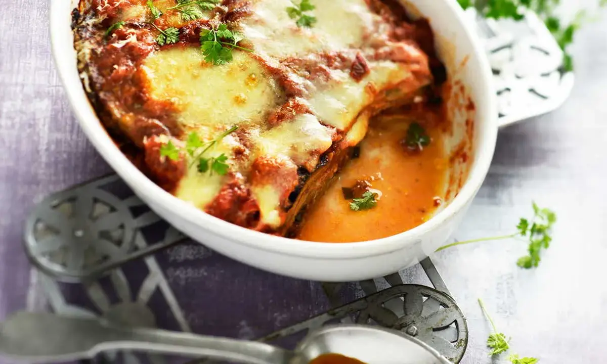 Un plat de recette parmigiana napolitaine gratinée, avec des aubergines, de la sauce tomate et du fromage fondant, garni de persil frais.
