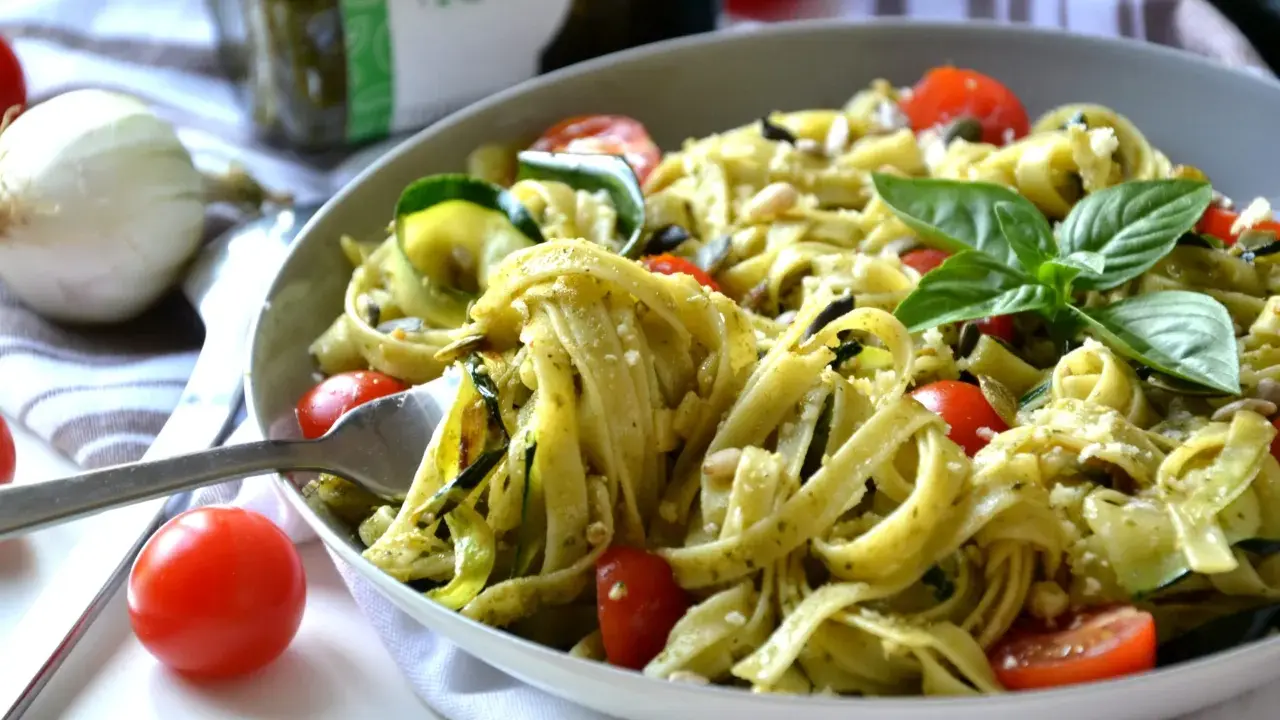 Un plat de tagliatelles de courgettes, tomates cerises et pesto, garni de basilic frais et de pignons de pin.