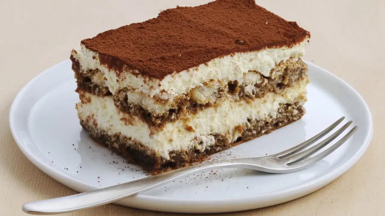 Une part de tiramisu sans oeuf, légère et aérienne, saupoudrée de cacao, sur une assiette blanche avec une fourchette.