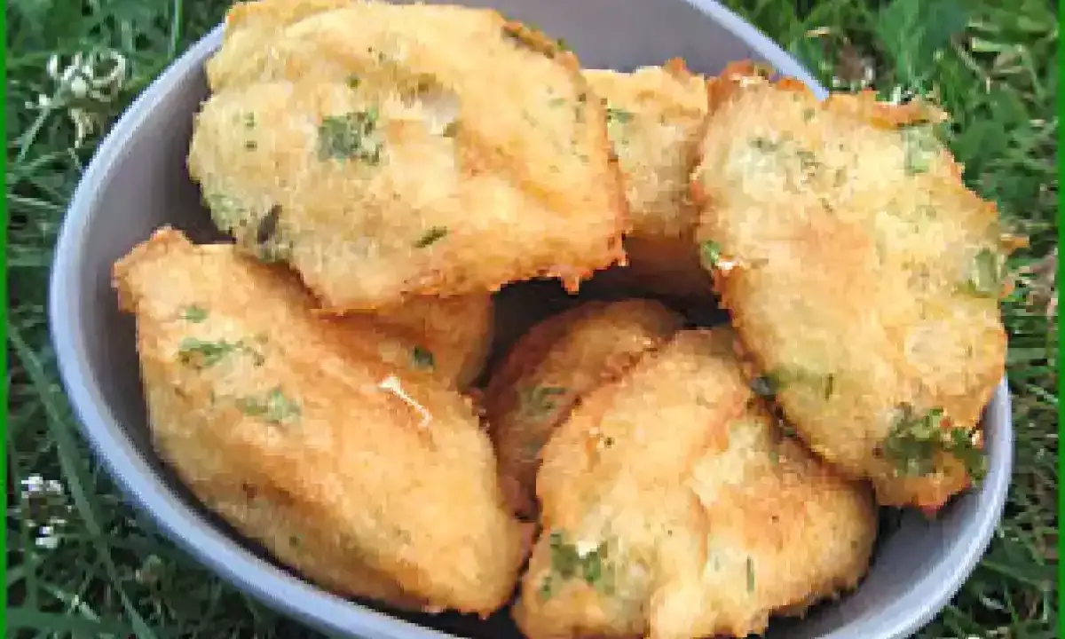 Un bol rempli de beignets de morue portugais dorés, parsemés d'herbes vertes, sur un fond d'herbe.