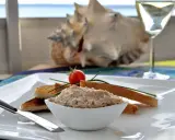 Un bol de rillettes de maquereau, servi avec des toasts grillés, une tomate cerise et un verre de vin blanc.