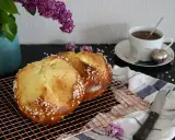 Deux pains briochés, parfaits pour une mouna recette, refroidissent sur une grille. Une tasse de thé et des lilas complètent la scène.