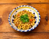 Un plat de pois chiches cuisinés avec des carottes et des oignons, garni de coriandre fraîche. La cuisson pois chiche est réussie, le plat est appétissant.