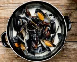 Un plat de moules à la crème, prêtes à être dégustées, sur une table en bois rustique.