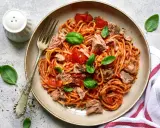 Assiette de pâtes au thon, sauce tomate et basilic frais. Un plat simple et savoureux prêt à être dégusté.