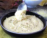 Une cuillère sert une portion généreuse de polenta crémeuse, assaisonnée de poivre noir, dans un bol. Une recette polenta réconfortante.