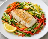 Filet de julienne poêlé, servi avec un mélange coloré de légumes coupés en julienne et un quartier de citron.