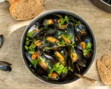 Un plat généreux de moules marinières, garni de persil frais, avec du pain de campagne à côté.