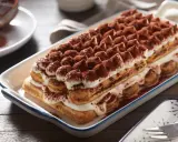 Un délicieux tiramisu, un dessert italien parfait pour un boudoir gourmand, est présenté dans un plat rectangulaire, saupoudré de cacao.