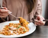 Une personne mange des spaghettis à la sauce tomate et au parmesan avec deux fourchettes.