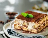 Un délicieux tiramisu anniversaire, saupoudré de cacao et garni d'une feuille de menthe fraîche, prêt à être dégusté.