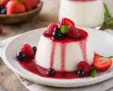 Panna cotta, un dessert italien dont l'origine remonte au début du XXe siècle, servi avec un coulis de fruits rouges et des baies fraîches.