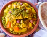 Un plat de tajine poulet aux olives, petits pois et carottes, garni de piments verts. Accompagné de pain.