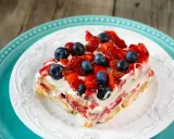 Tranche de tiramisu aux fruits rouges, garnie de fraises et myrtilles fraîches, sur une assiette blanche ornée.