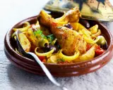 Un plat de tajine poulet citron, avec des morceaux de poulet dorés, des olives, des oignons et des tomates, servi dans un plat en terre cuite.