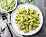 Assiette de pâtes rigatoni généreusement enrobées de pesto vert vif, avec un bol de sauce à côté. Un délice de pâtes au pesto !