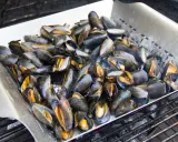 Un plateau de moules au barbecue, prêtes à être dégustées. Les coquilles sombres et orangées s'entrouvrent sous l'effet de la chaleur.