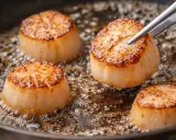 Quatre belles coquilles Saint-Jacques poêlées dans une poêle, dorées et juteuses, prêtes à être dégustées.